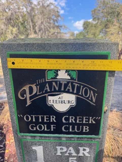 On-site fabrication planning at The Plantation at Leesburg: measuring an existing course monument with a tape measure to design a QR-enabled plaque insert, produced in-house by Happy Path Studios.